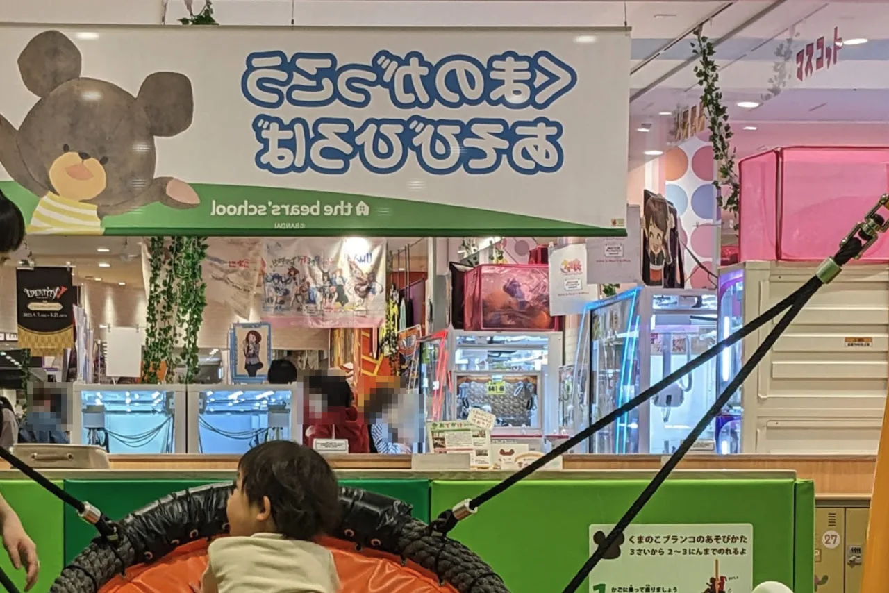 くまのがっこうあそびひろばの入口。ジャッキーのイラストが描かれた看板と、かごのブランコ