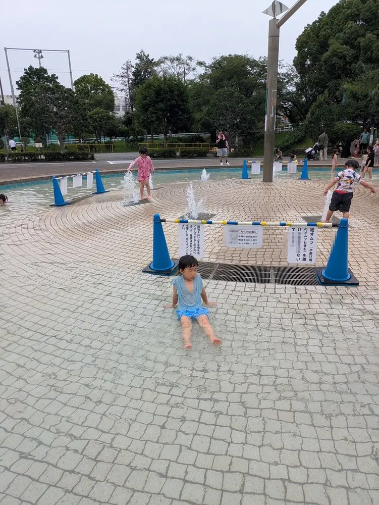 公園の噴水広場を歩く子ども。青いコーンで区切られた円形の広場