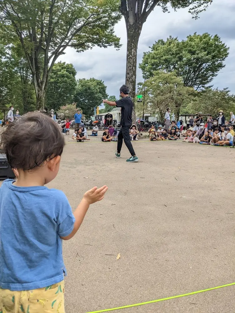 広い砂地の広場。手前に子ども、奥に大勢の人が集まっている