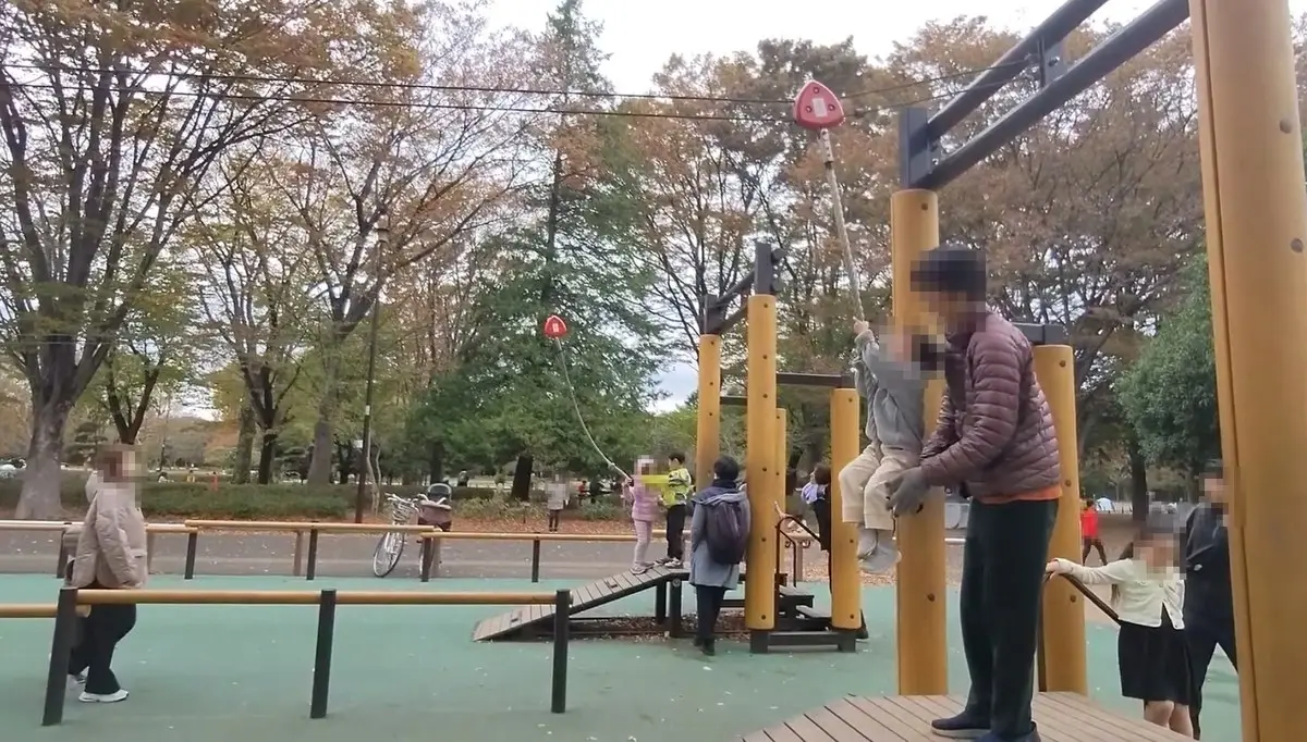 木製のターザンロープで遊ぶ親子。周囲は紅葉した木々と大勢の来園者