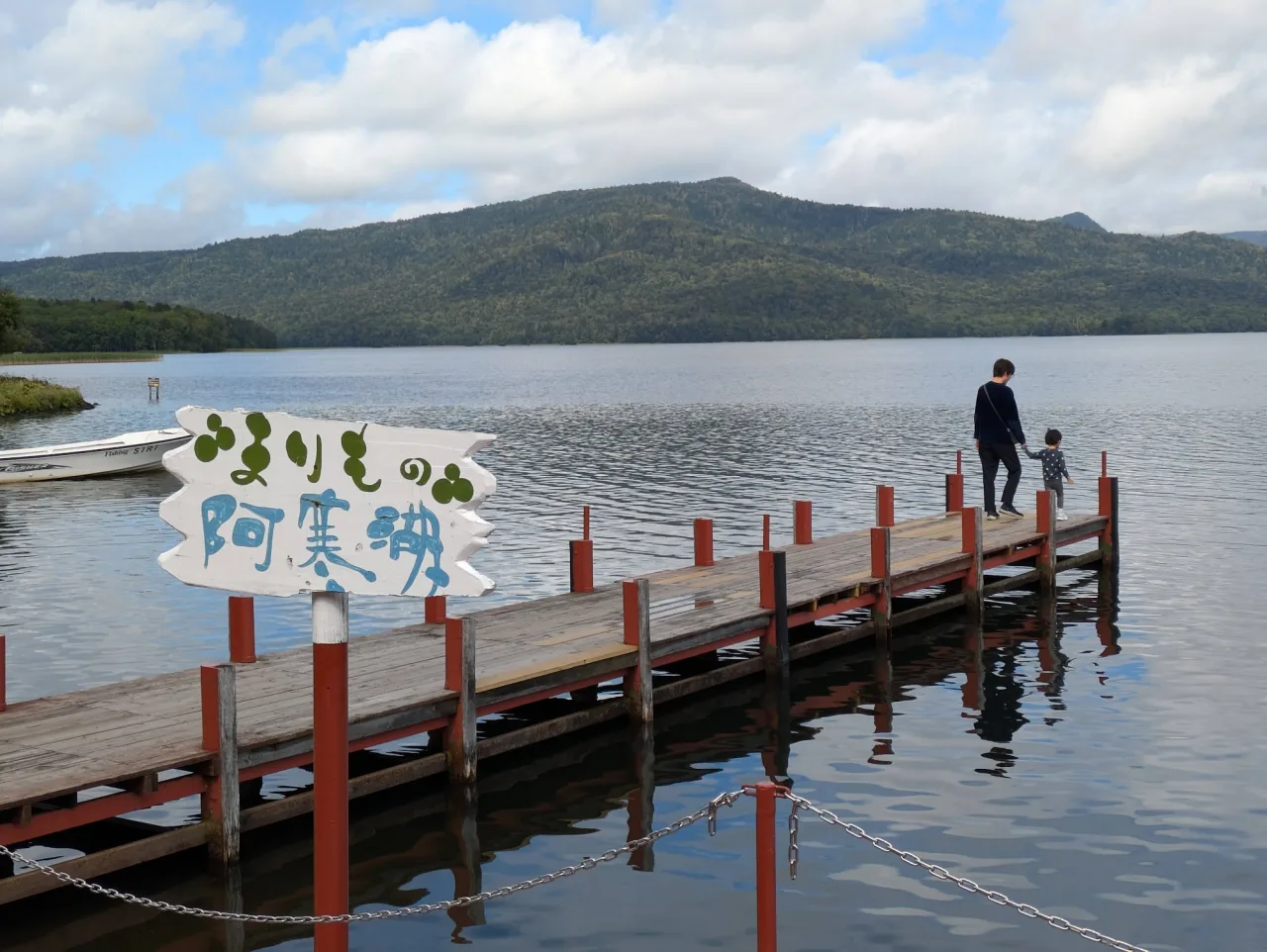 「まりもの阿寒湖」の看板と、湖に伸びる赤い柱の桟橋。奥に雄阿寒岳